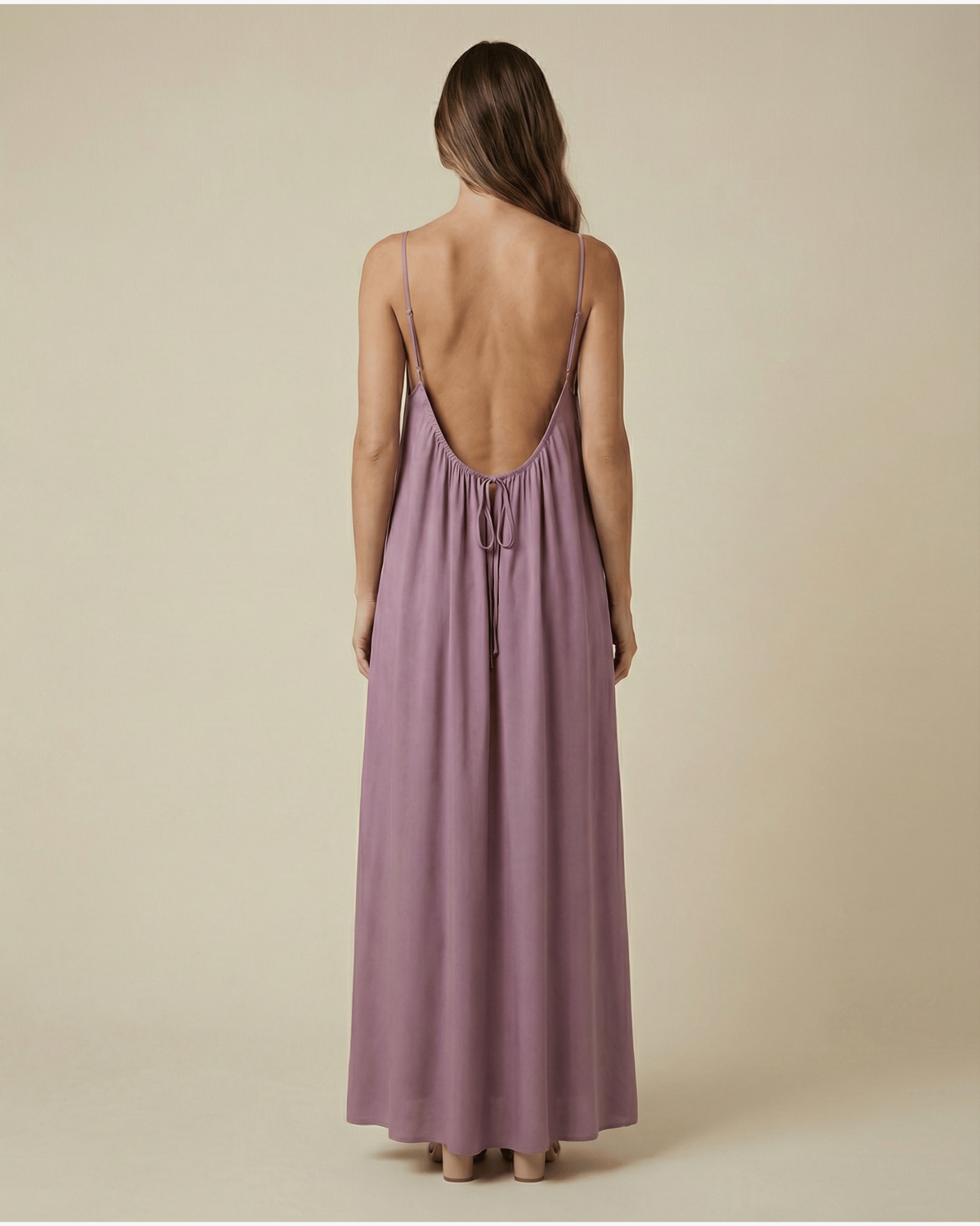 Woman wearing a long, light purple dress with thin straps on a beige background