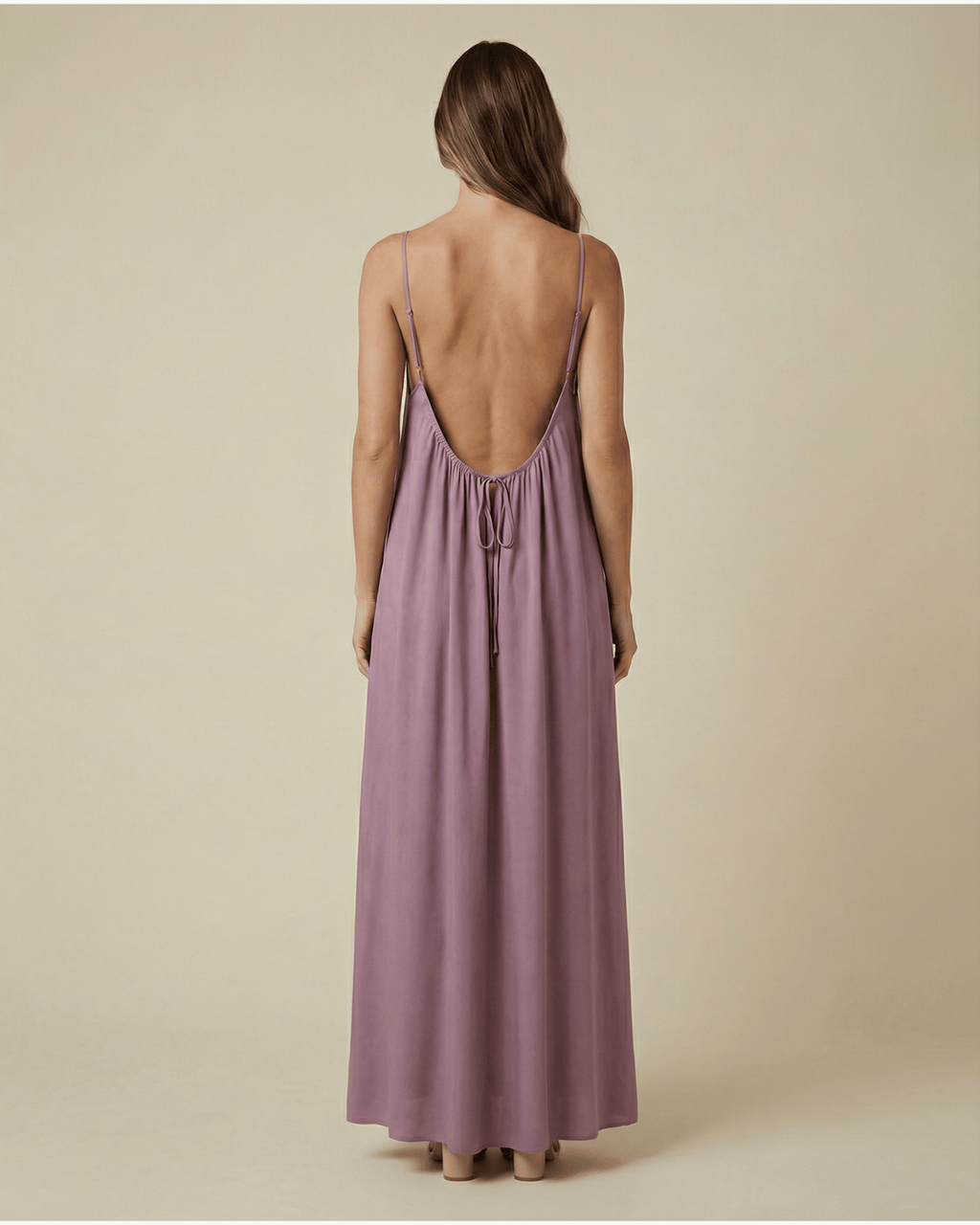 Woman wearing a long, light purple dress with thin straps on a beige background