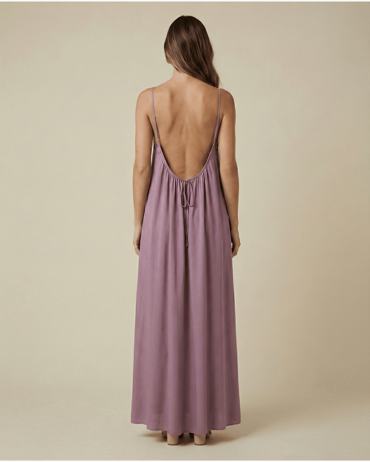 Woman wearing a long, light purple dress with thin straps on a beige background