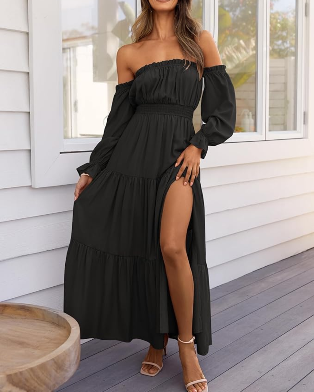 Woman wearing a black off-shoulder dress with a high slit on a wooden deck.