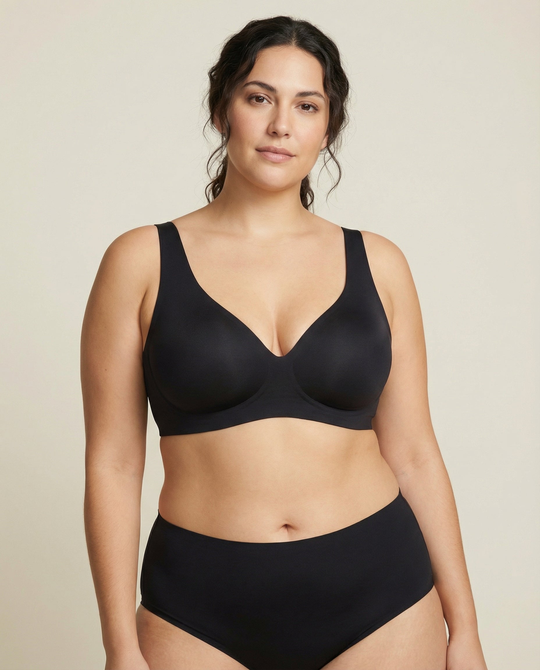 Woman wearing a black bra and underwear set against a beige background