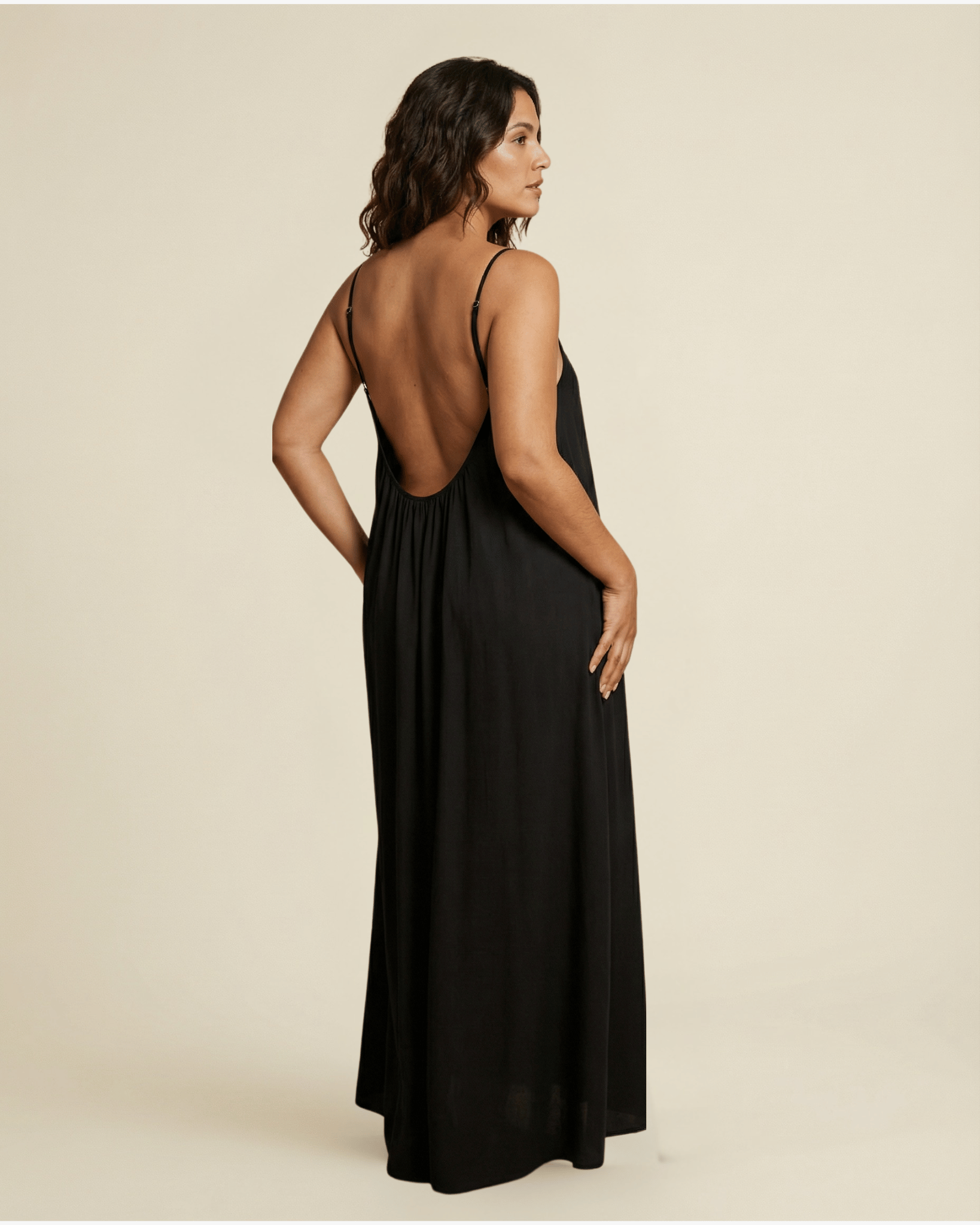Woman wearing a black dress with an open back on a beige background