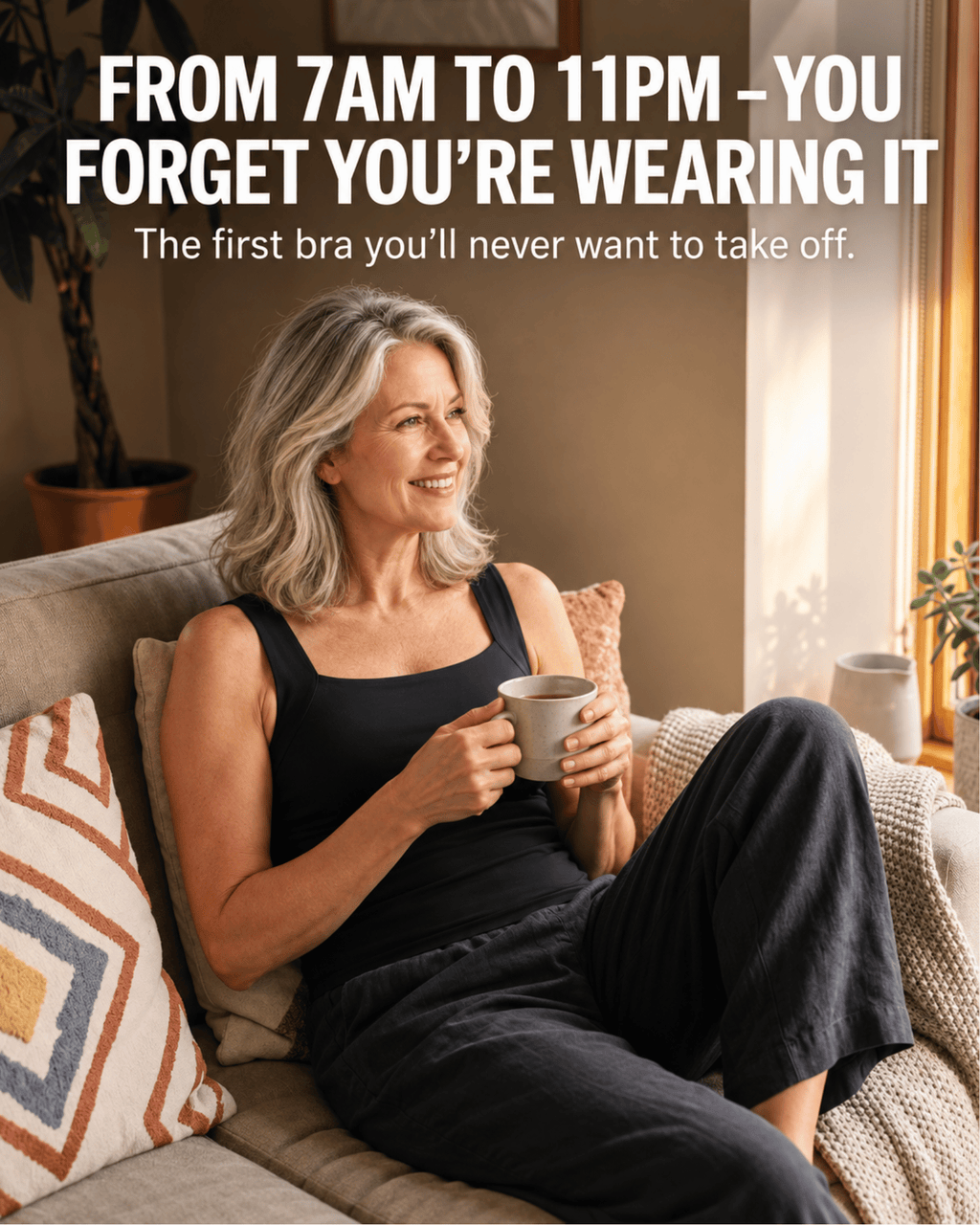 A smiling woman with gray hair sits on a beige couch in a sunlit living room, wearing a black sleeveless bra and dark pants while holding a mug. Large white text at the top reads, 'FROM 7AM TO 11PM - YOU FORGET YOU'RE WEARING IT.
