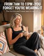 A smiling woman with gray hair sits on a beige couch in a sunlit living room, wearing a black sleeveless bra and dark pants while holding a mug. Large white text at the top reads, 'FROM 7AM TO 11PM - YOU FORGET YOU'RE WEARING IT.