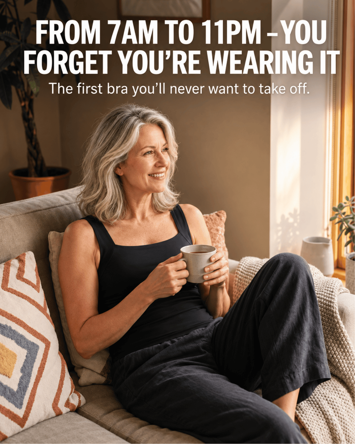A smiling woman with gray hair sits on a beige couch in a sunlit living room, wearing a black sleeveless bra and dark pants while holding a mug. Large white text at the top reads, 'FROM 7AM TO 11PM - YOU FORGET YOU'RE WEARING IT.