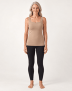 A woman stands barefoot against a plain light background wearing a fitted sleeveless beige top and black leggings.