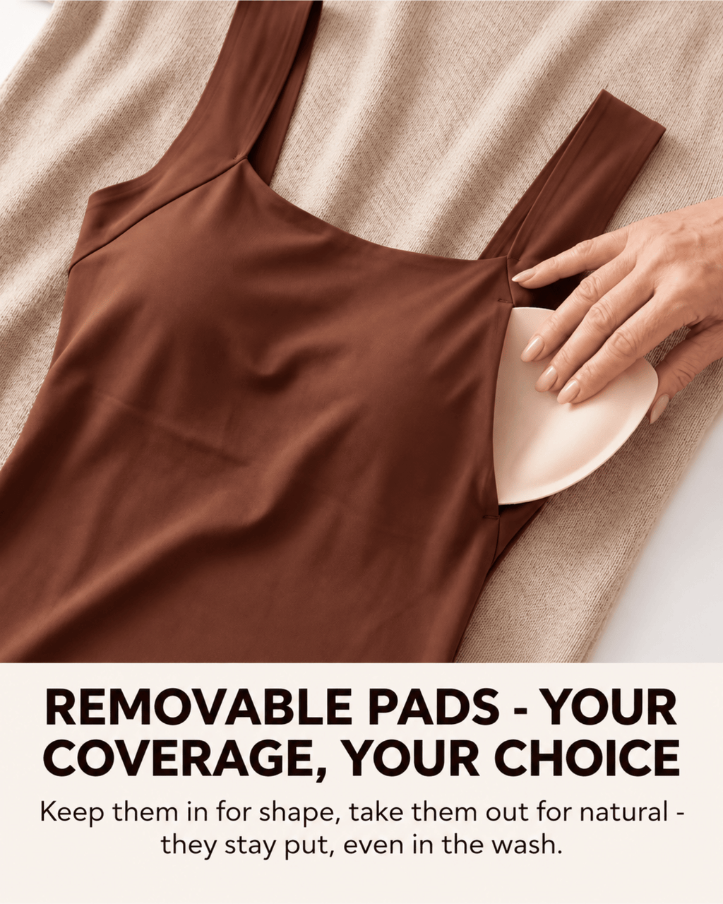 A brown camisole-style top laid flat on a beige textured blanket, with a hand placing a light beige removable bra pad into one of the shoulder cutouts. Large text at the bottom reads: 'REMOVABLE PADS - YOUR COVERAGE, YOUR CHOICE' with smaller supporting text below.