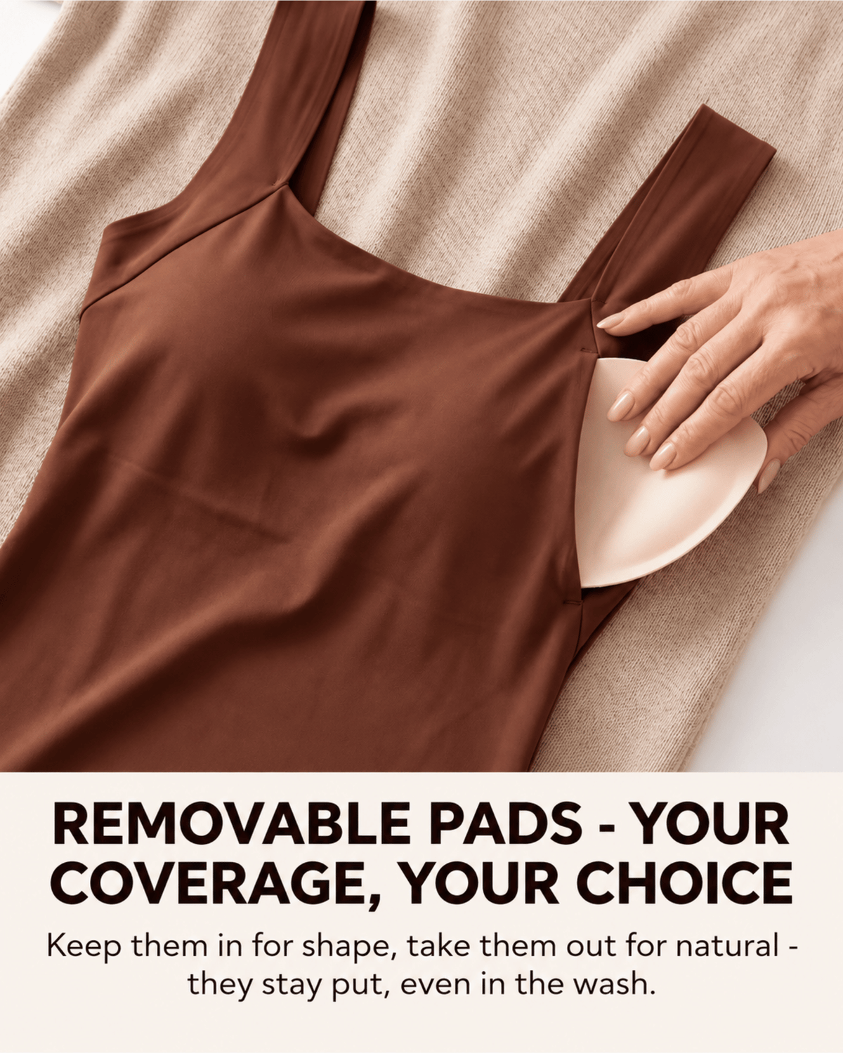A brown camisole-style top laid flat on a beige textured blanket, with a hand placing a light beige removable bra pad into one of the shoulder cutouts. Large text at the bottom reads: 'REMOVABLE PADS - YOUR COVERAGE, YOUR CHOICE' with smaller supporting text below.