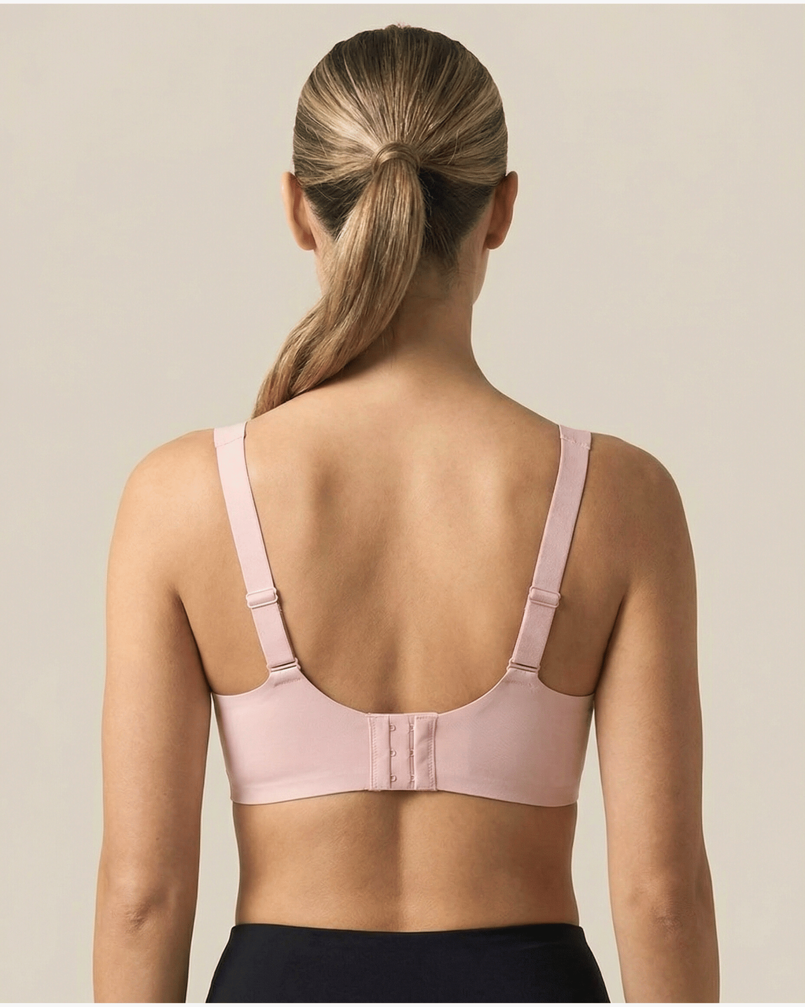 Woman wearing a light pink bra against a beige background