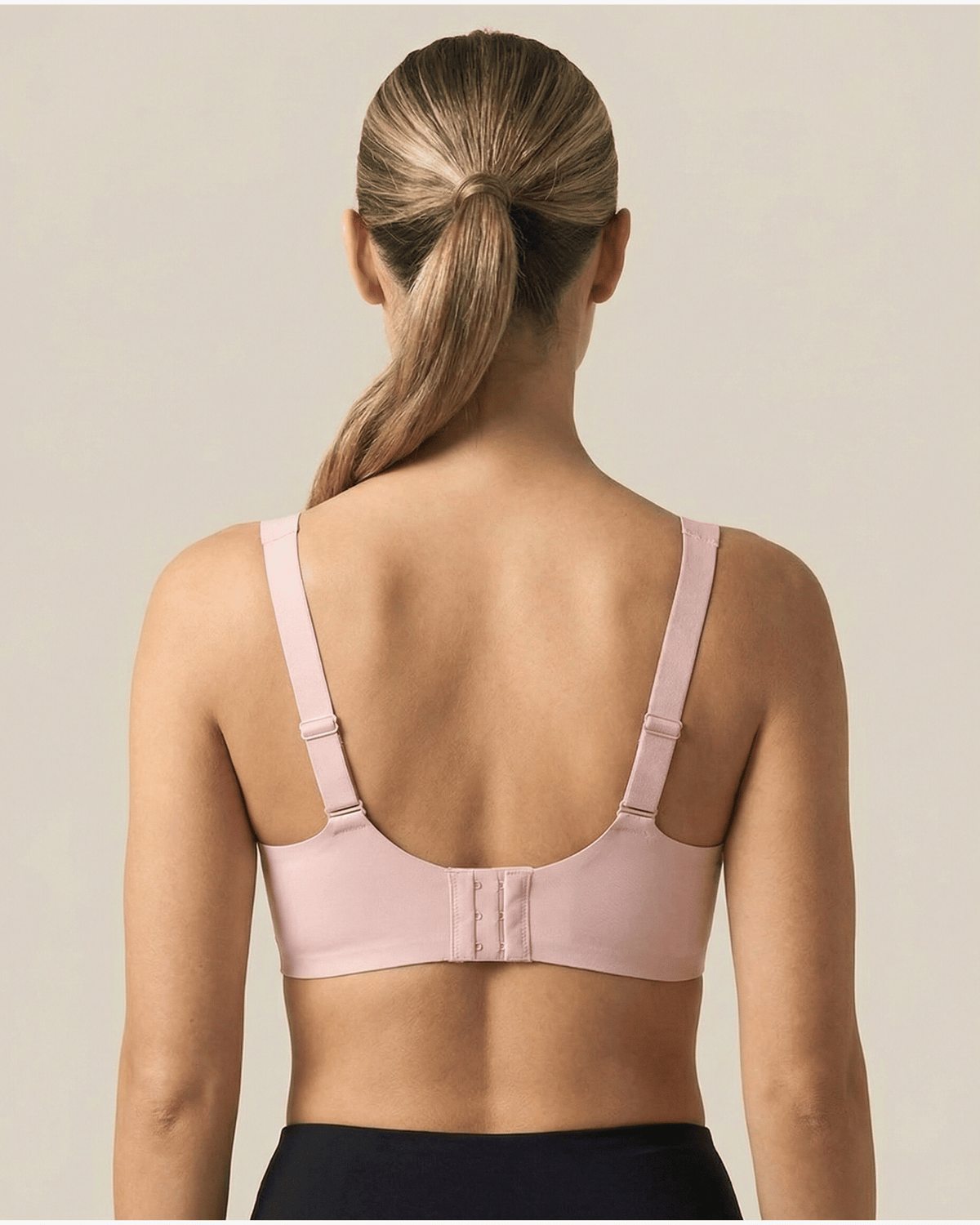 Woman wearing a light pink bra against a beige background