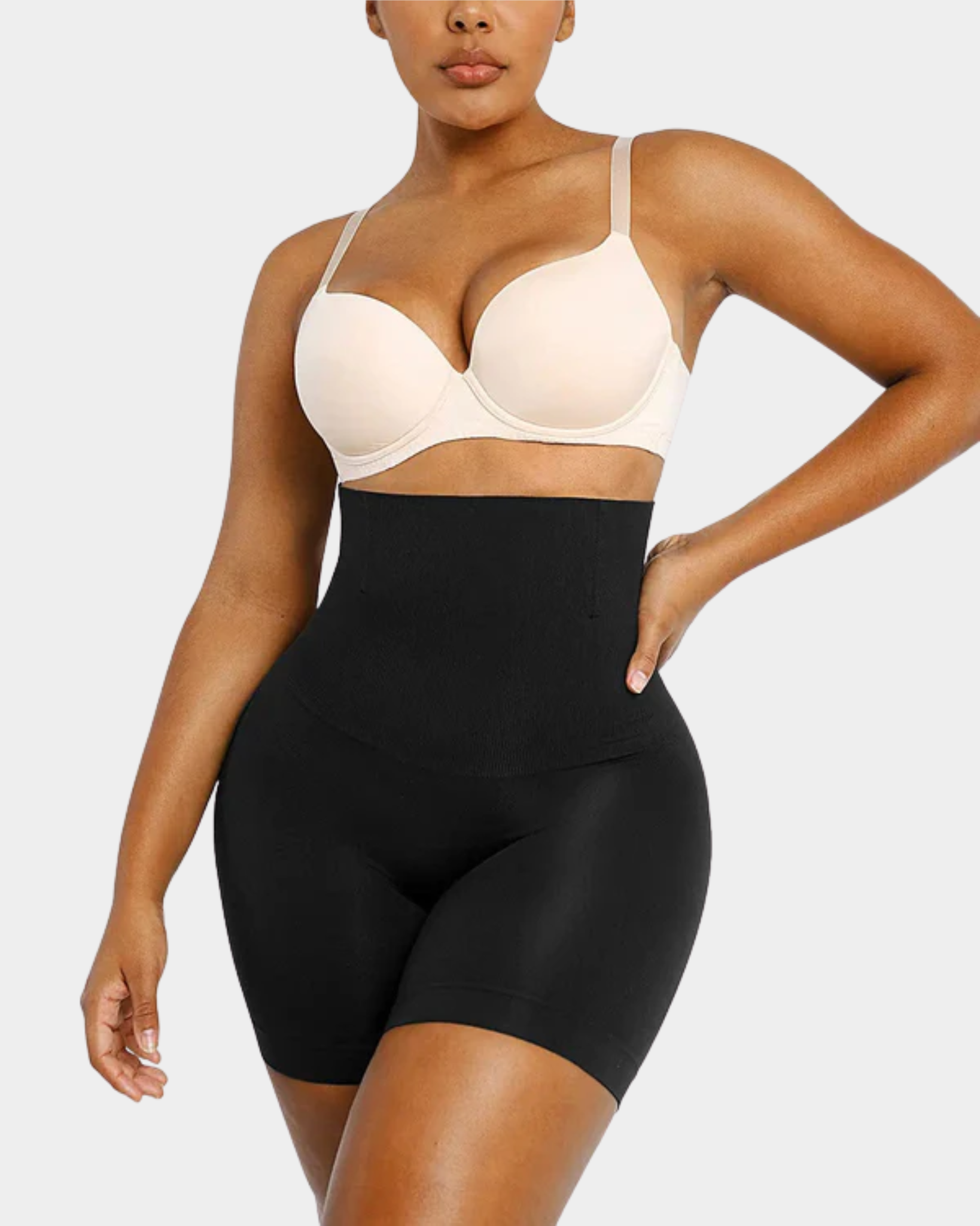 Person wearing a beige bra and black shapewear on a plain background
