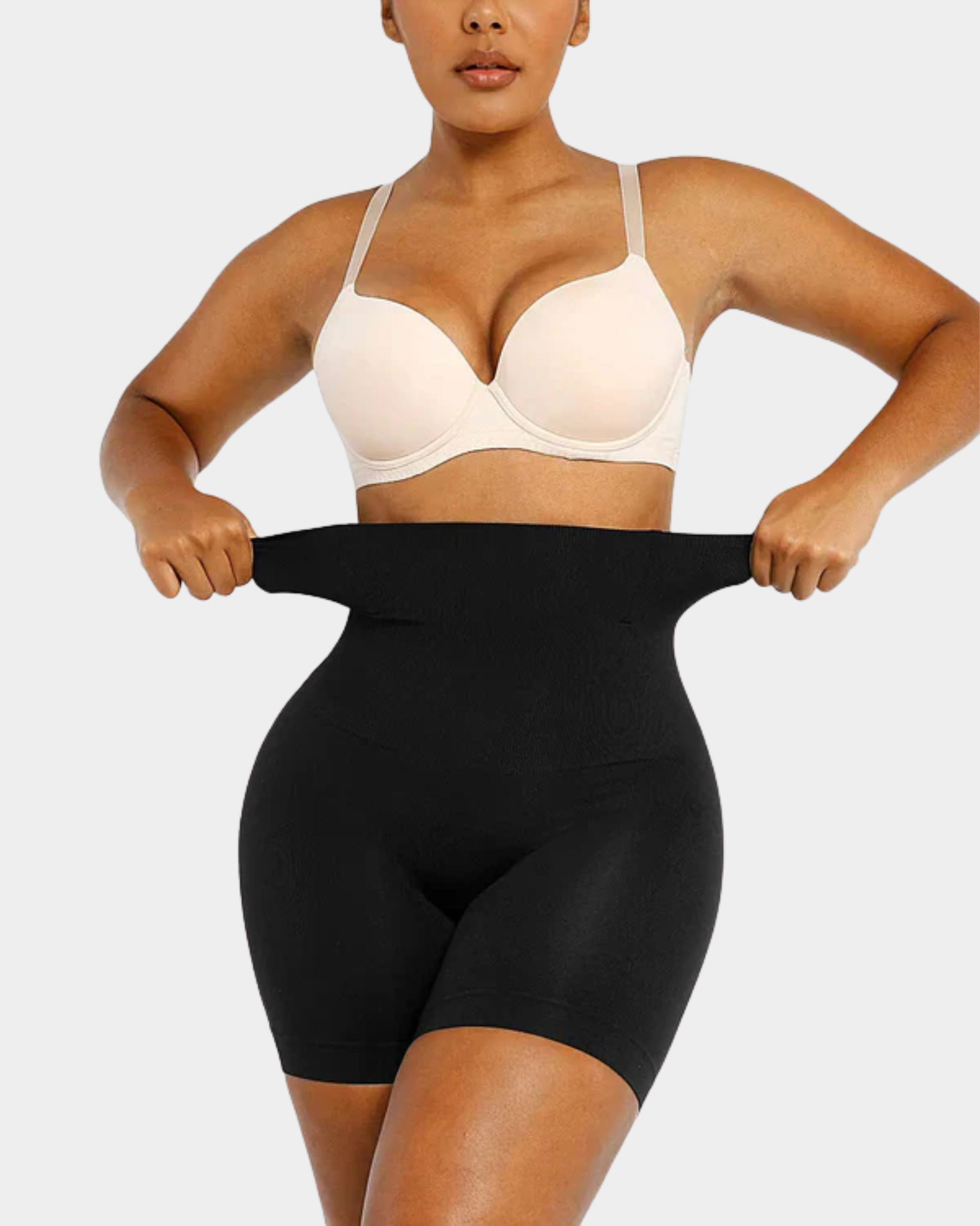 Person wearing a beige bra and black shapewear on a plain background