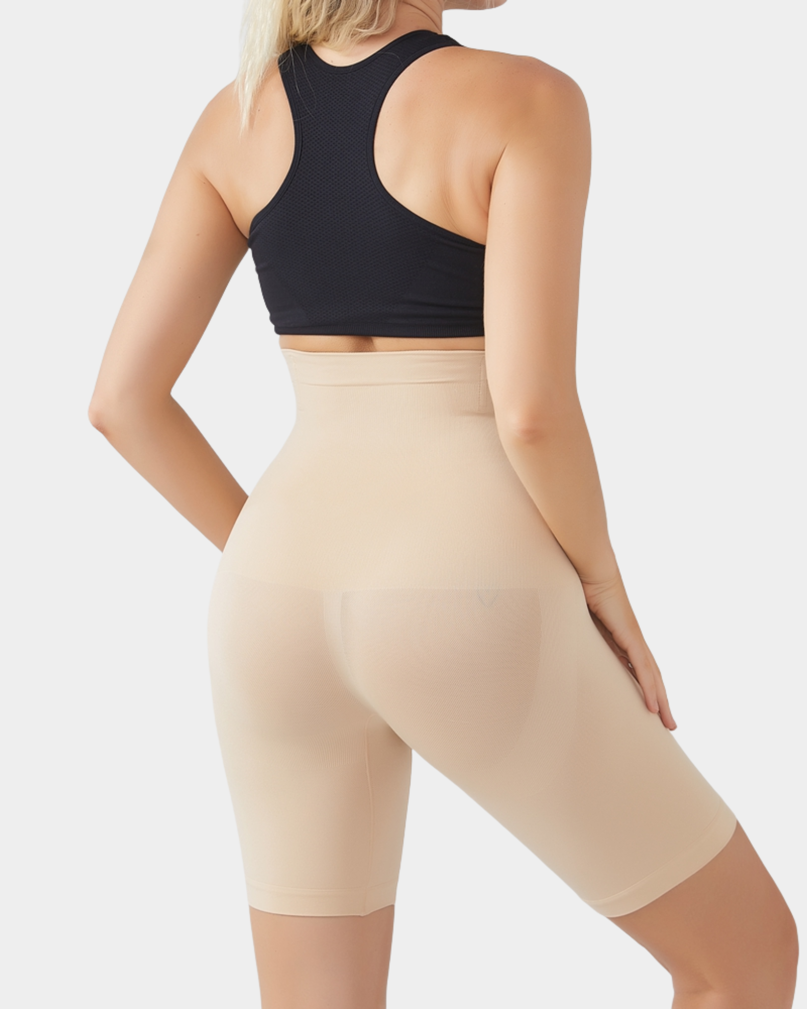 Woman wearing a black sports bra and beige shapewear on a white background