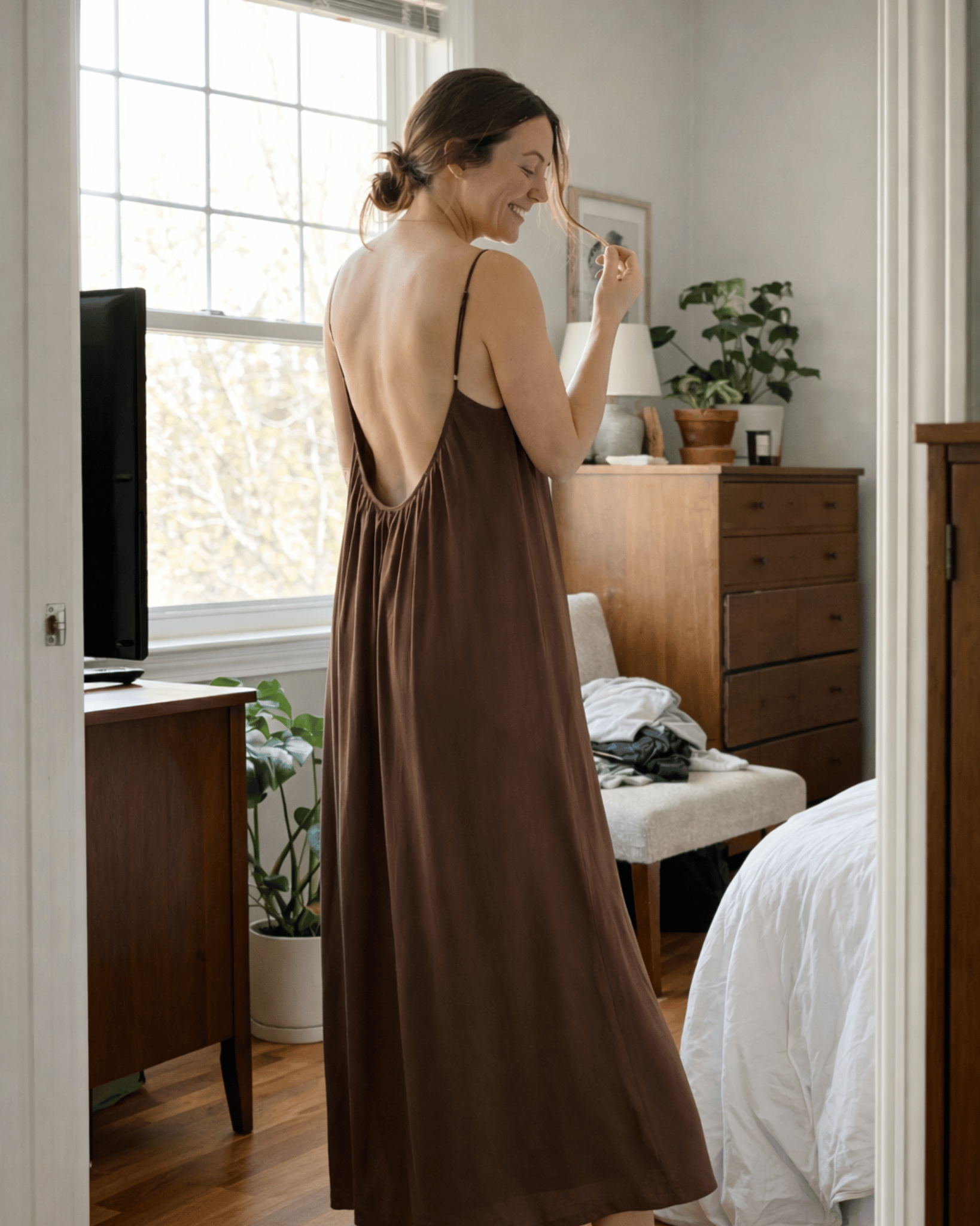 Woman in a brown dress standing in a bedroom taking a photo of herself.